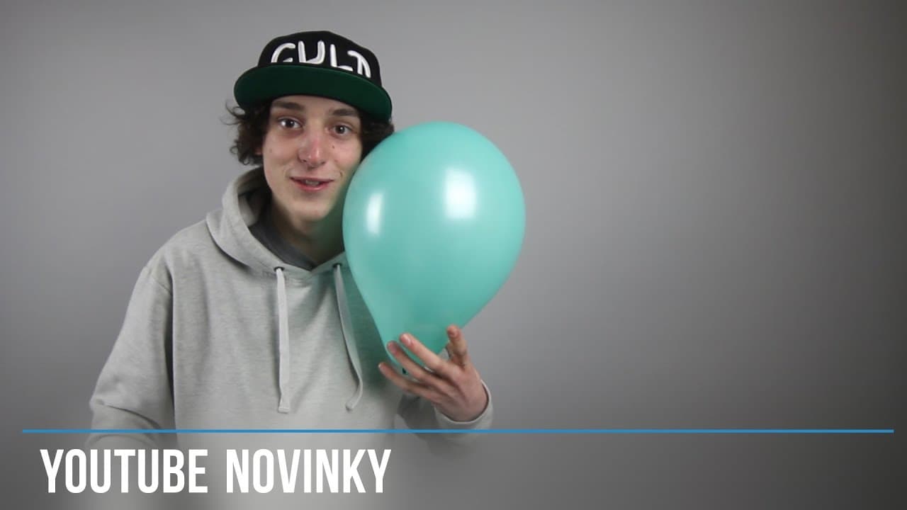 Mladý člen erem drží tyrkysový balónek před neutrálním pozadím.